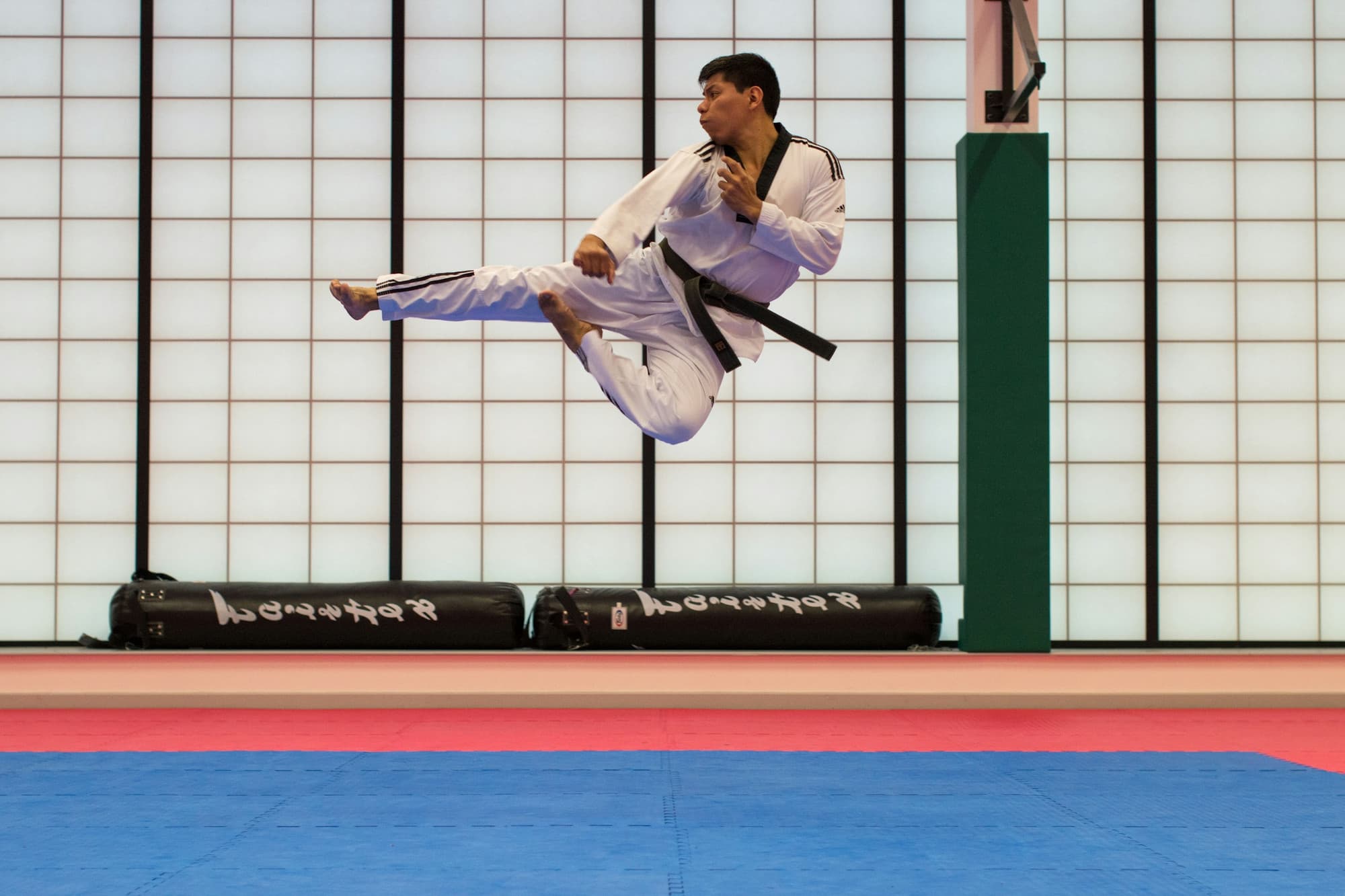 Pratiquant d'arts martiaux en kimono effectuant un coup de pied sauté dans un dojo